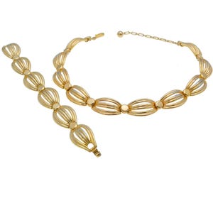 May include: A gold-tone necklace and bracelet set with a delicate, woven design. The jewelry features a series of oval-shaped links with a textured, striped pattern.
