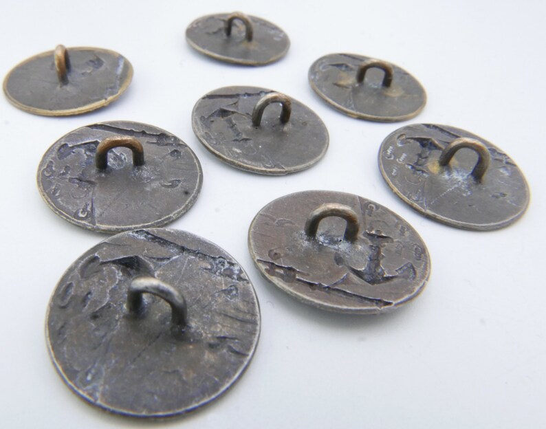 May include: Eight antique silver-toned buttons with a loop on the top. The buttons have a worn, aged appearance and are circular in shape.