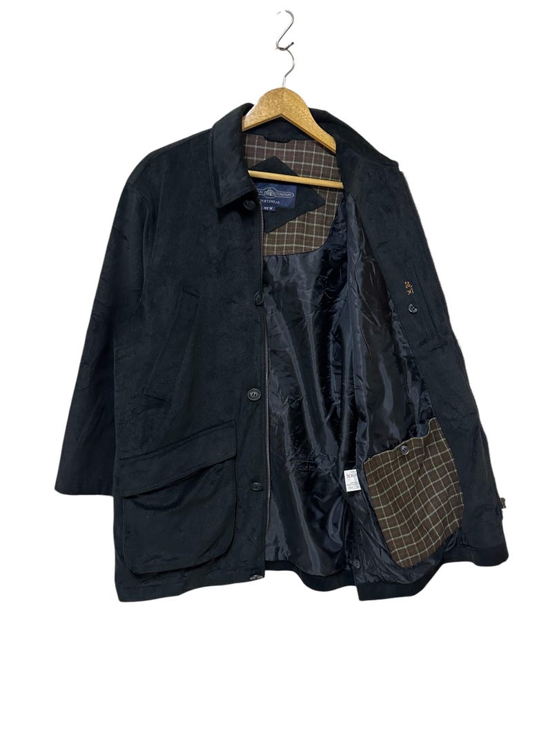 May include: A black corduroy jacket with a button fastening and a plaid lining. The jacket has a large pocket on the front and a smaller pocket on the inside.