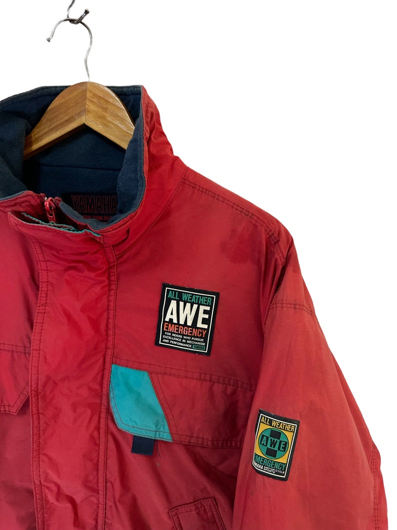 May include: Red Yamaha jacket with a blue and teal accent. The jacket has two patches that say "All Weather AWE Emergency" with the Yamaha logo.