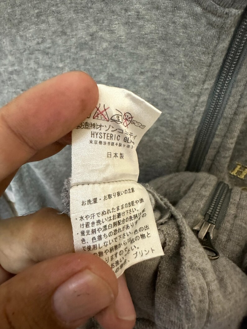 May include: Close-up of a gray cotton garment tag with black text. The tag reads "株オゾンコミティ HYSTERIC GL 東京都渋谷区千駄ヶ谷3 日本製" and includes washing instructions in Japanese.