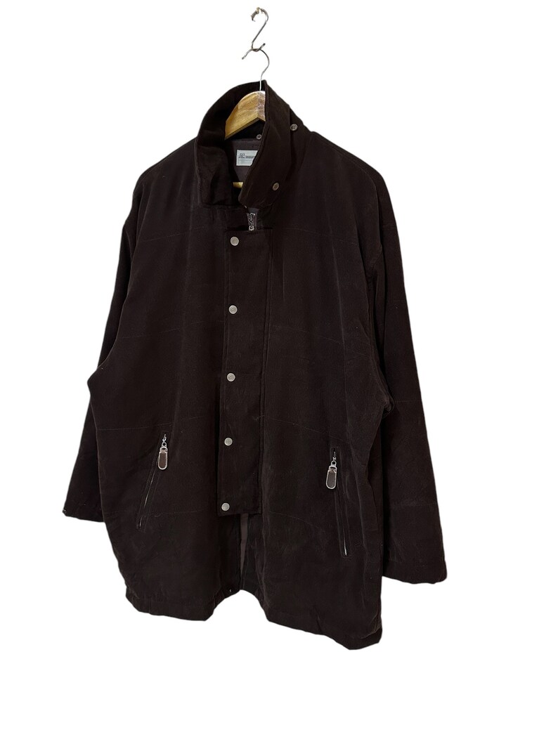 May include: A dark brown jacket with a high collar, a zip closure, and multiple pockets. The jacket has a slightly oversized fit and a relaxed silhouette.