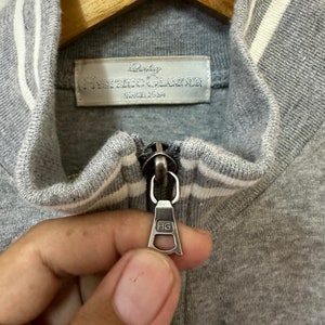 May include: Close-up of a gray zipper on a gray and white striped jacket. The zipper pull has the letters "HG" on it. The label on the jacket reads "Baby Hysteric Glamour Since 1989".