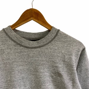 以下が含まれることがあります： 左胸に小さな刺繍ロゴが付いたグレーのスウェットシャツです。