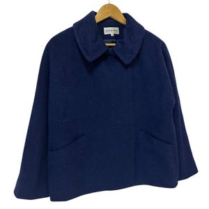 May include: A navy blue wool jacket with a wide collar and two front pockets. The jacket is hanging on a wooden hanger. The brand name "HANAE MORI" is visible on a tag inside the collar.