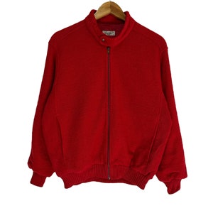 Puede incluir: Una chaqueta roja con cremallera, cuello y puños de canalé. La chaqueta tiene una pequeña etiqueta en el lado izquierdo del cuello que dice "Ralph Lauren".