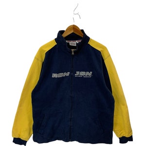 Op de afbeelding: Een blauw en geel zip-jack met de tekst "Ron Jon Surf Shop" in zilveren letters.