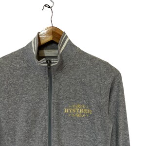 May include: A gray zip-up sweatshirt with a white striped collar and a gold embroidered logo that says "HYSTERIC".