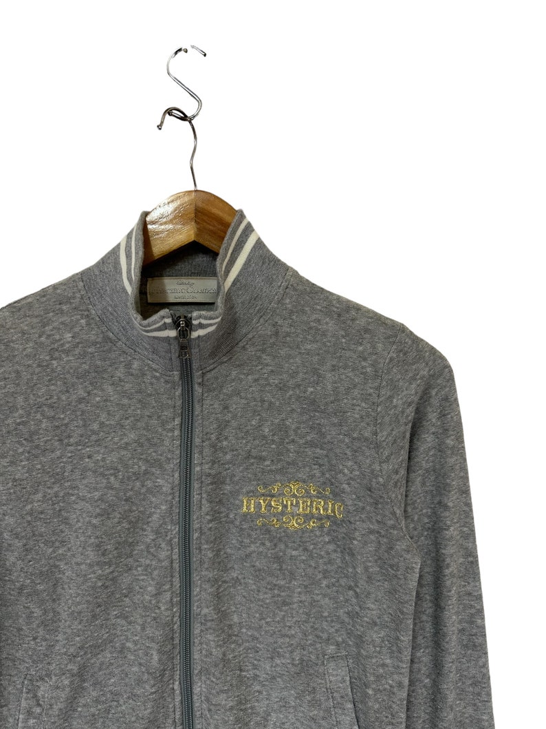 May include: A gray zip-up sweatshirt with a white striped collar and a gold embroidered logo that says "HYSTERIC".
