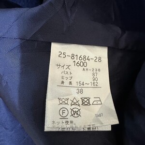May include: Close-up of a navy blue garment's interior, revealing a label with Japanese text and numbers. The label includes measurements for bust (87 cm), hip (90 cm), and height (154-162 cm). The number 38 is also visible.