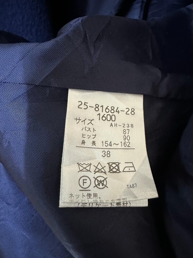 May include: Close-up of a navy blue garment's interior, revealing a label with Japanese text and numbers. The label includes measurements for bust (87 cm), hip (90 cm), and height (154-162 cm). The number 38 is also visible.