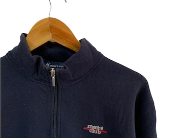 May include: Navy blue fleece pullover with a quarter-zip closure and a mock neck. The garment features the embroidered text "men's club" in red and white. The pullover is hanging on a wooden hanger.