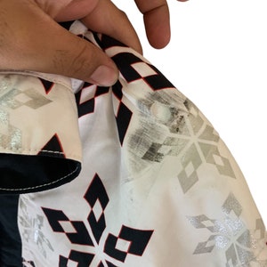May include: White button-up shirt with a black and red snowflake pattern. The shirt has a white collar and a black button closure.