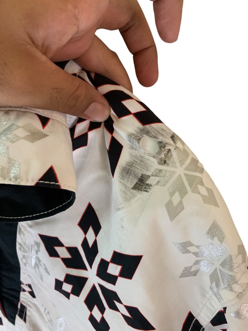 May include: White button-up shirt with a black and red snowflake pattern. The shirt has a white collar and a black button closure.