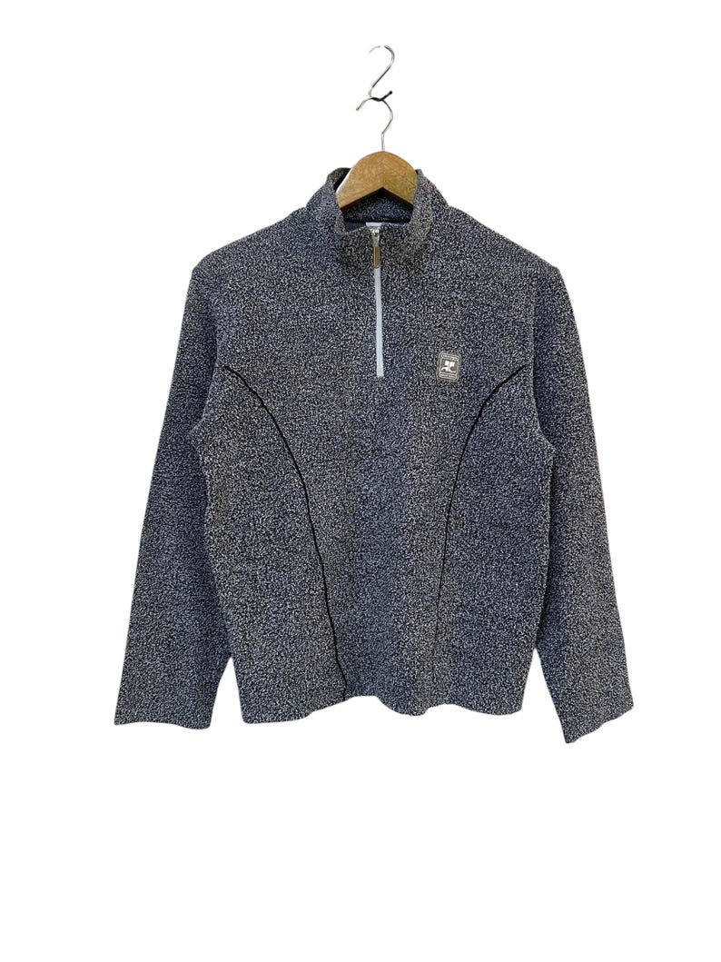 May include: A gray fleece pullover with a half-zip closure and a small logo patch on the chest. The long-sleeved top has a textured appearance and is hanging on a wooden hanger.