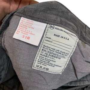 May include: A gray corduroy pant leg with a white care label that reads "Machine wash cold. Inside out. Do not bleach. Tumble dry low. Laver &agrave; la machine &agrave; l'eau froide, &agrave; l'envers. Ne pas javelliser. S&eacute;cher &agrave; la machine cycle doux." The label also includes the brand name "AG Adriano Goldschmied" and "Made in U.S.A."