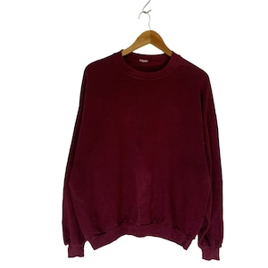 May include: A maroon crew neck sweatshirt with long sleeves. The sweatshirt is hanging on a wooden hanger.