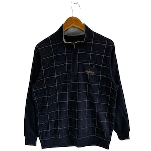 May include: A navy blue long-sleeved sweater with a white checkered pattern and a zipper closure. The sweater has a small pocket on the left chest with a brown leather patch.