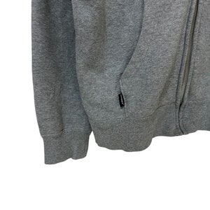 May include: A gray zippered hoodie with a kangaroo pocket and a small black "remark" label on the pocket.