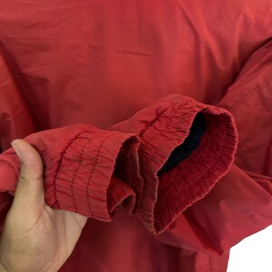 May include: A red windbreaker jacket with a zip fastening and elasticated cuffs. The jacket is made from a lightweight fabric and has a relaxed fit.