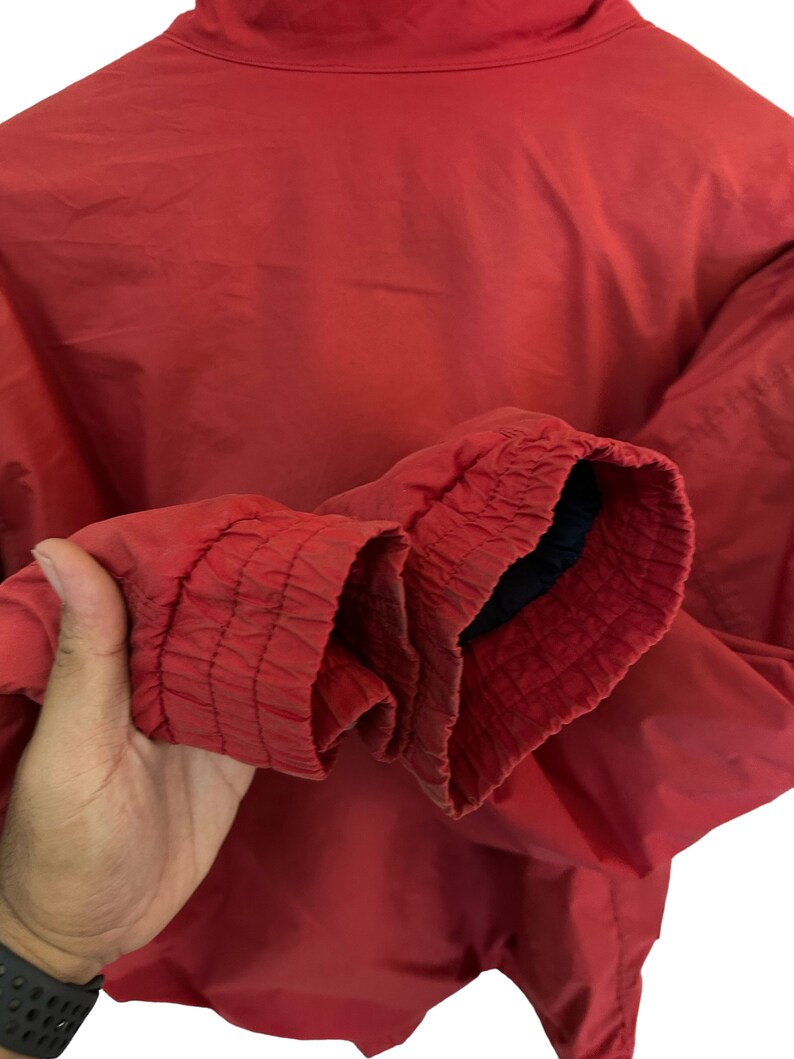 May include: A red windbreaker jacket with a zip fastening and elasticated cuffs. The jacket is made from a lightweight fabric and has a relaxed fit.