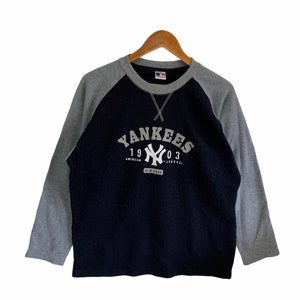 May include: A navy blue and grey long-sleeved sweatshirt with a white graphic of the New York Yankees logo and text that reads "Yankees 1903 American League New York".