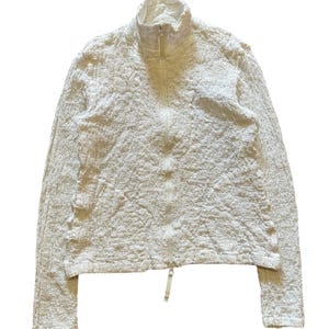 May include: Off-white textured zip-up jacket with a high collar. The jacket has a unique, crinkled appearance and a full-length zipper. The sleeves are long, and the overall style is casual and comfortable.