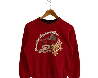 Può includere: Felpa rossa a maniche lunghe con una stampa grafica di una tavola da surf, palme e fiori. Il testo "Hawaiian Longboard Wear" e "Piko" è stampato sulla felpa.