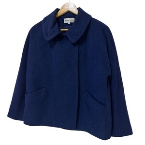 May include: A navy blue wool coat with a wide collar and two front pockets. The coat is hanging on a wooden hanger. The coat is a cropped style.