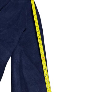 May include: A navy blue wool coat with a button closure and a collar. A yellow measuring tape shows the coat's length. The coat's sleeve is approximately 23 inches long.