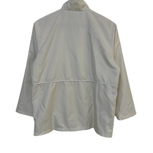 May include: A cream-colored jacket with a stand-up collar and long sleeves. The jacket has a white horizontal stripe across the midsection and is hanging on a wooden hanger. The back of the jacket is visible.
