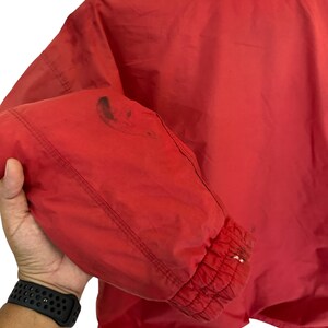 May include: Red windbreaker jacket with a zip fastening and elasticated cuffs. The jacket has a small stain on the left sleeve.