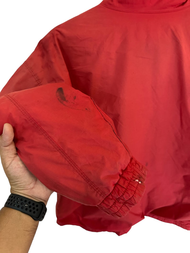 May include: Red windbreaker jacket with a zip fastening and elasticated cuffs. The jacket has a small stain on the left sleeve.