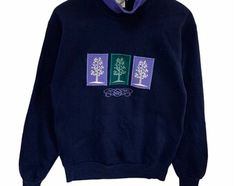 May include: A navy blue sweatshirt with a mock neck and a design of three trees in purple, green, and white. The trees are framed in purple rectangles.