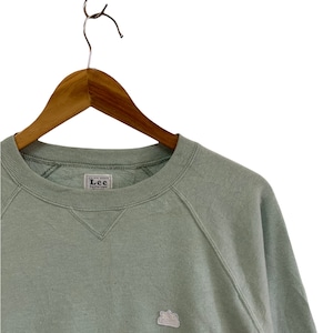 May include: A light green sweatshirt with a small embroidered logo on the left chest. The logo is a crown with the letters "Lee" inside. The sweatshirt has a crew neck and raglan sleeves.