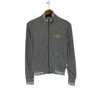 May include: A gray zip-up jacket with white ribbed trim on the cuffs and waistband. The jacket has a gold embroidered logo that says "HYSTERIC" on the front.