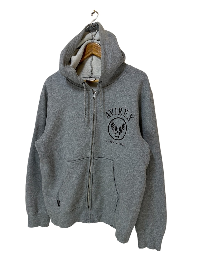 May include: A gray zip-up hoodie with a black embroidered logo that says "AVIREX" and "U.S. ARMY AIR CORPS".