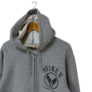 May include: A gray zip-up hoodie with a black Avirex logo featuring a winged star and the text "U.S. ARMY AIR CORPS".