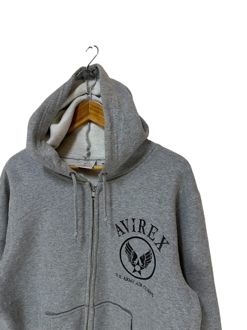 May include: A gray zip-up hoodie with a black Avirex logo featuring a winged star and the text "U.S. ARMY AIR CORPS".
