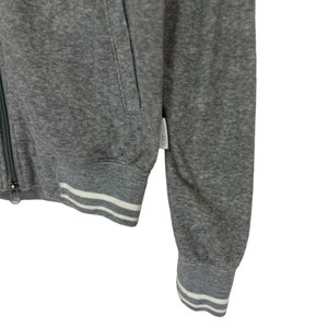 May include: A gray zip-up sweatshirt with white ribbed trim around the cuffs and bottom hem. The sweatshirt has a zipper closure and a pocket on the left side.