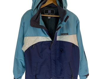 May include: A blue, white and navy blue hooded jacket with the word "ESTERO" on the front. The jacket has a zip closure and two pockets on the front.