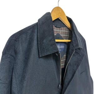 May include: A black zip-up jacket with a plaid lining. The jacket has a button closure and a zipper. The jacket is hanging on a wooden hanger.