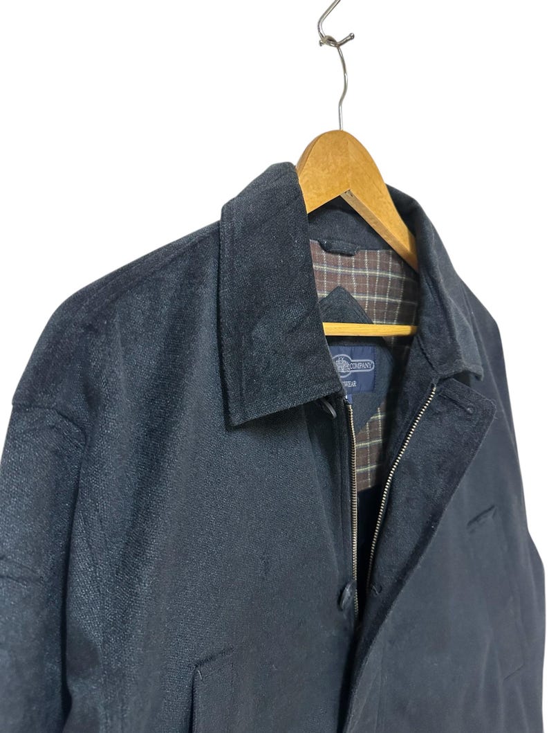 May include: A black zip-up jacket with a plaid lining. The jacket has a button closure and a zipper. The jacket is hanging on a wooden hanger.