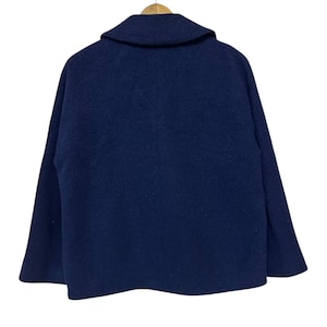 May include: A navy blue wool coat with a wide collar, hanging on a wooden hanger. The back of the coat is visible, showcasing its simple, classic design. The coat's fabric appears soft and has a slight texture.