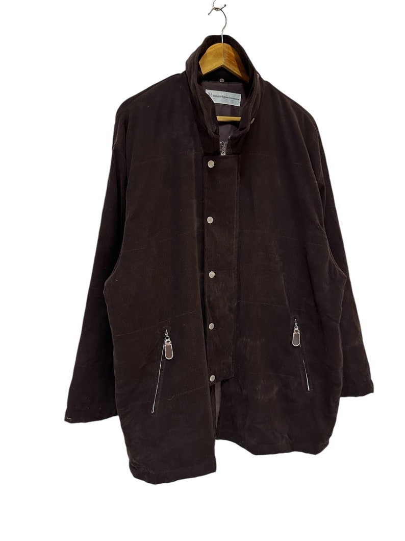 May include: A brown corduroy jacket with a zip and button fastening. The jacket has two zipped pockets on the front and a stand-up collar.