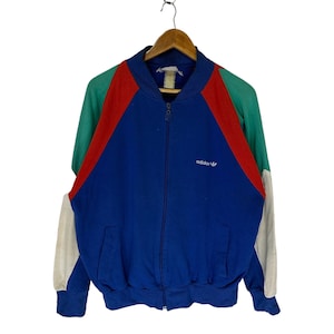May include: A blue, red, green, and white vintage Adidas zip-up jacket. The jacket has a white Adidas logo on the left chest.