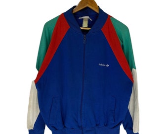 May include: A blue, red, green, and white vintage Adidas zip-up jacket. The jacket has a white Adidas logo on the left chest.