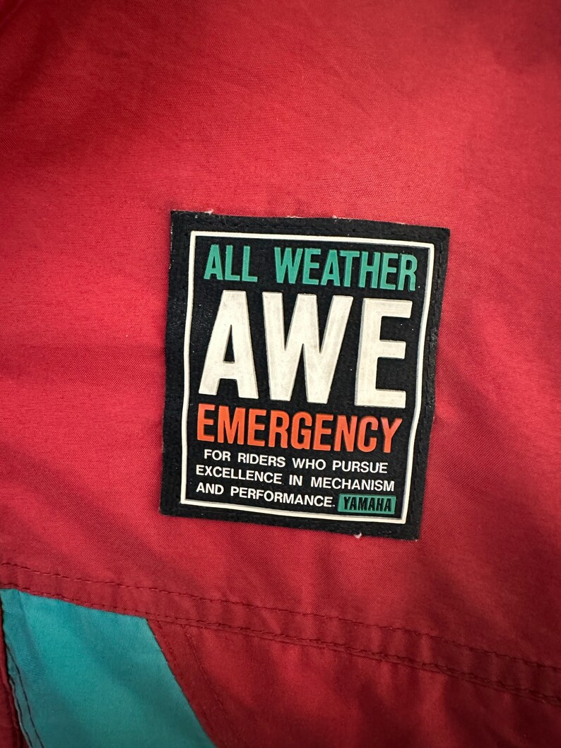 May include: A black and white patch with the text "ALL WEATHER AWE EMERGENCY" and "FOR RIDERS WHO PURSUE EXCELLENCE IN MECHANISM AND PERFORMANCE. YAMAHA".