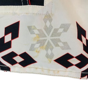 May include: White fabric with a black and red diamond pattern and a silver snowflake design. The fabric has a few yellow stains.