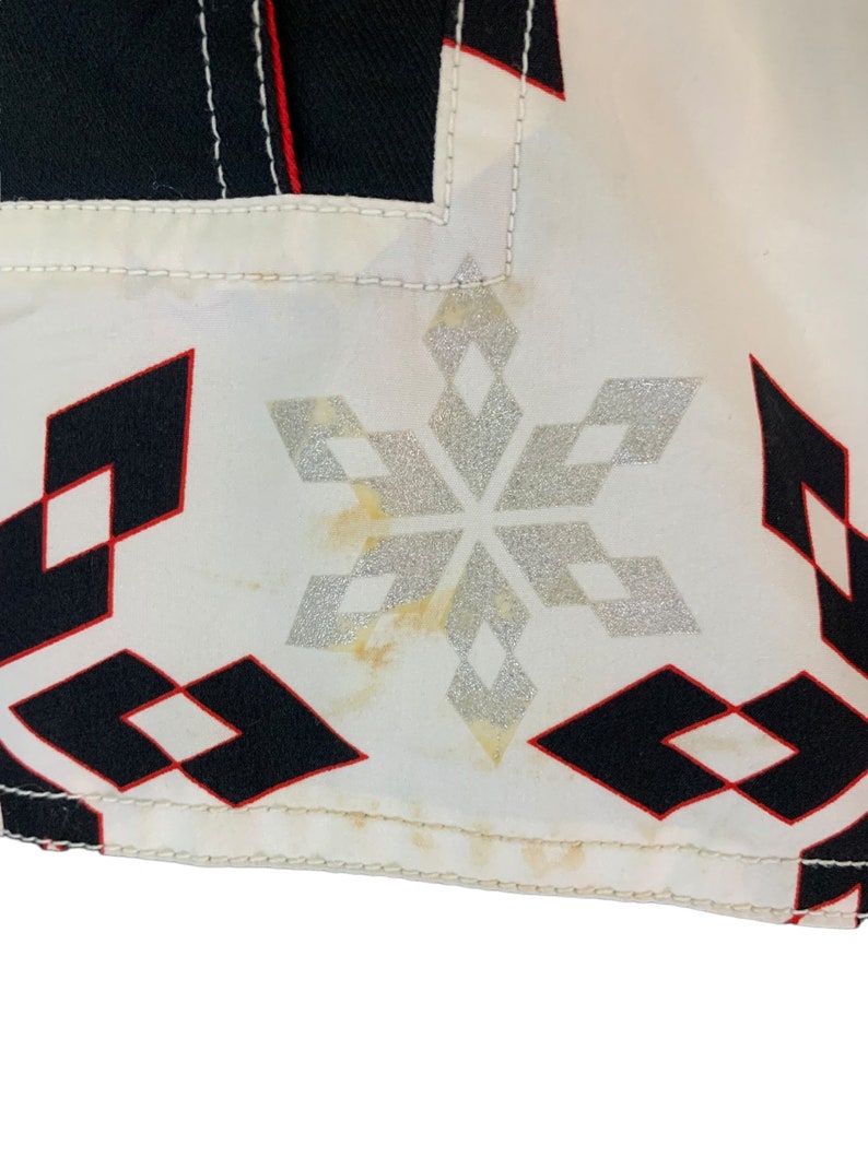May include: White fabric with a black and red diamond pattern and a silver snowflake design. The fabric has a few yellow stains.